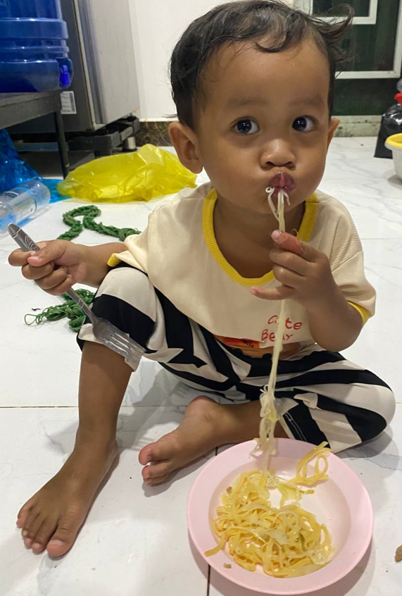 2-year-old boy eating noodles with a serious expression, refusing vegetables.