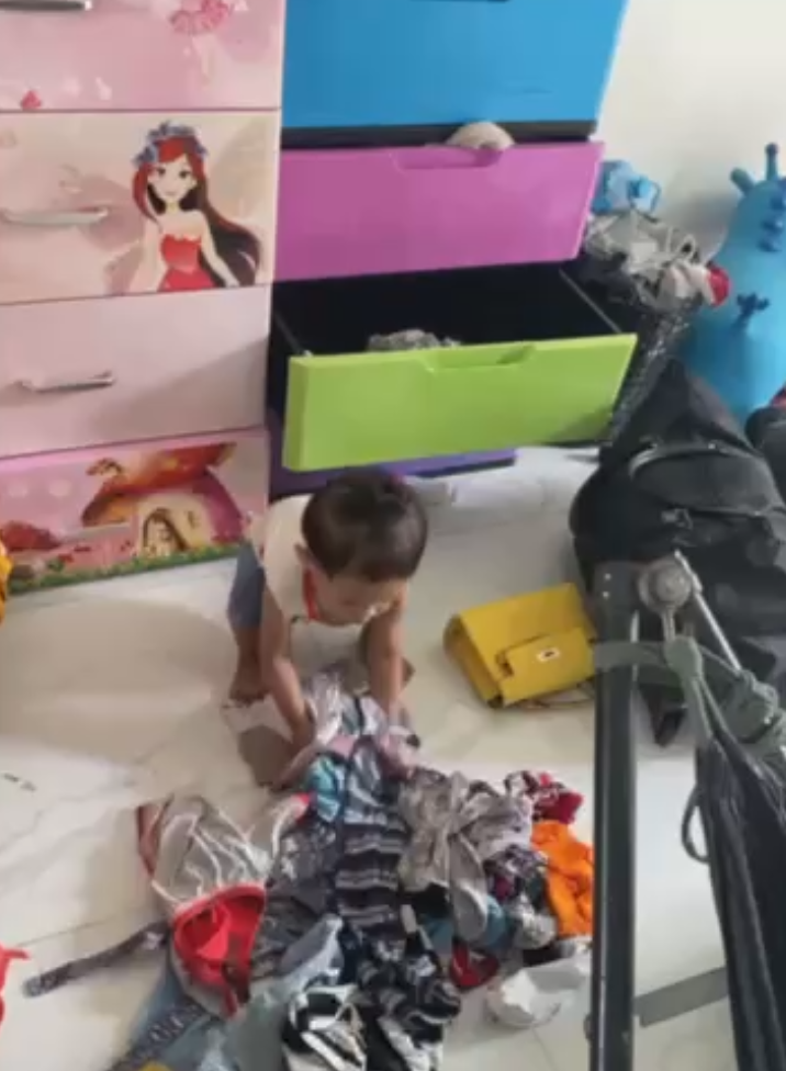 Toddler standing in front of colorful plastic storage drawers, preparing to pull clothes out of the green drawer.