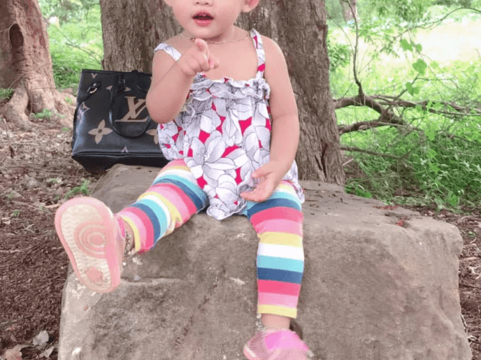 A confident young girl sits on a dusty rock and points her finger directly at the camera, demonstrating childhood resilience and determination.