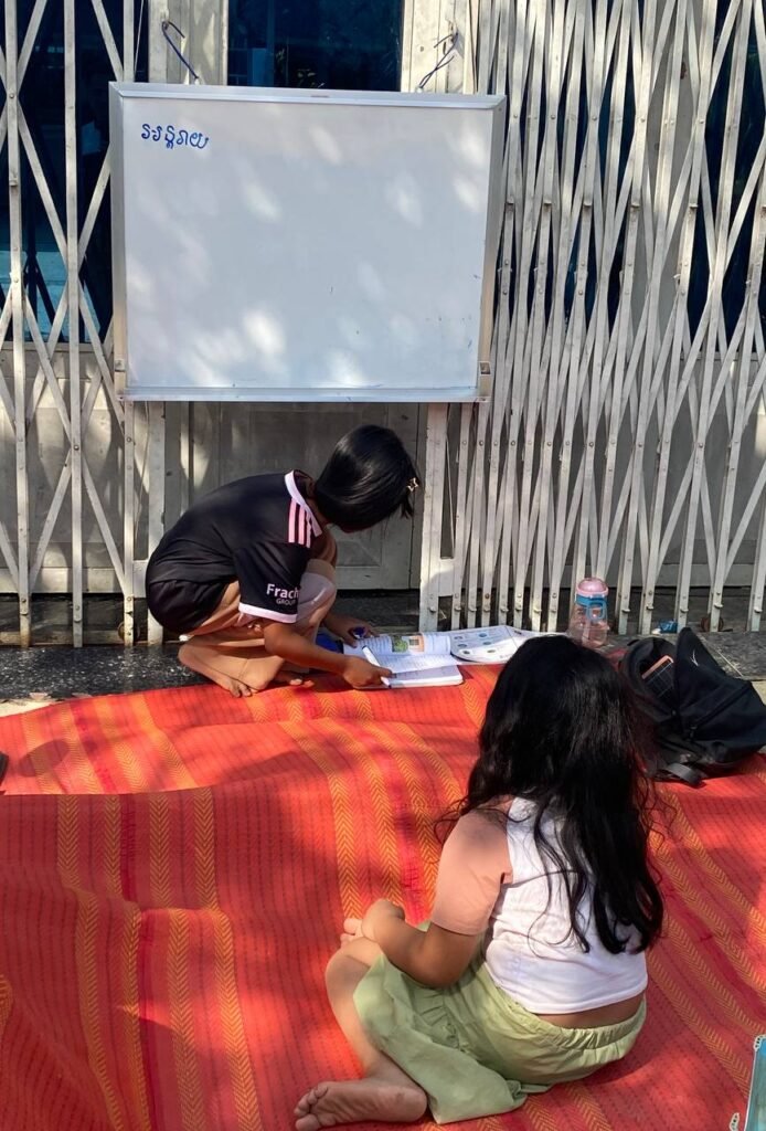 A young girl sitting on a mat focused on writing in her notebook during a pretend play lesson.