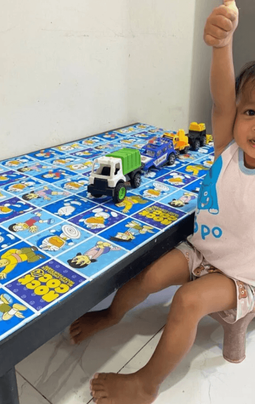 A happy toddler giving two thumbs up and smiling after successfully fixing his broken toy truck.