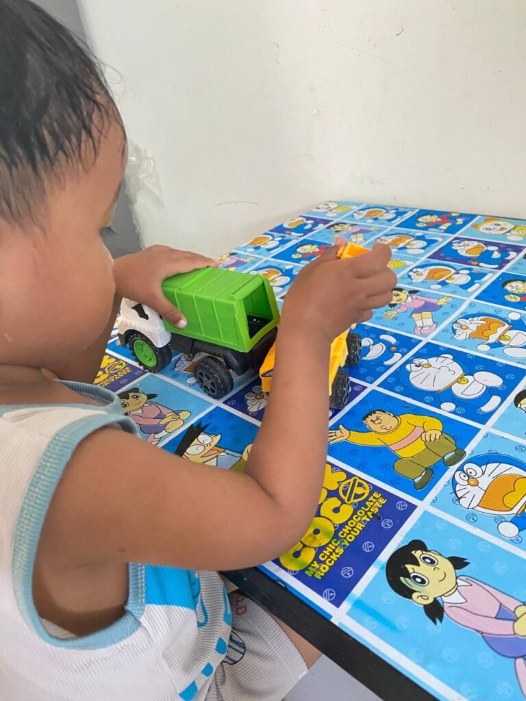 A child exploring the dumping mechanism of a green toy truck on a blue Doraemon table.