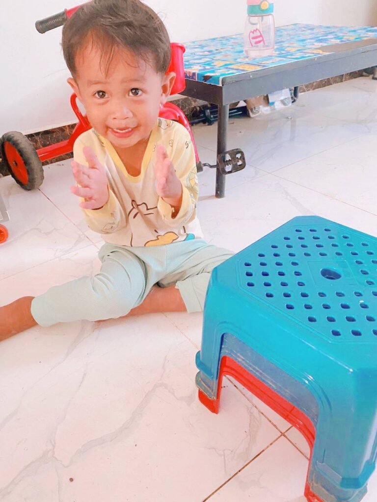 Happy toddler sitting on the floor clapping his hands after successfully stacking toys.