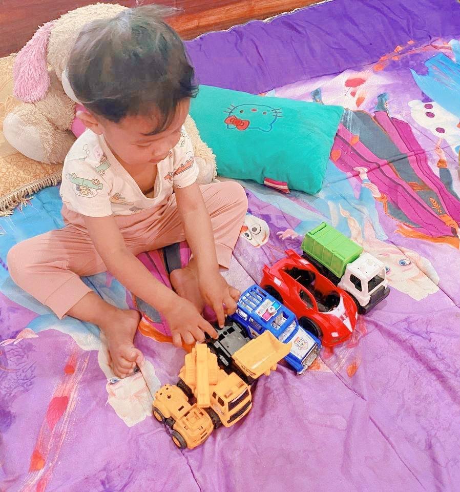 Toddler concentrating on parking a yellow toy truck in a precise spot, demonstrating fine motor skills and planning.