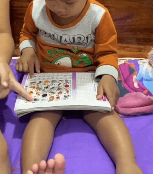 A parent's finger pointing to an animal picture in a colorful busy book while a toddler watches, playing the point and name game.
