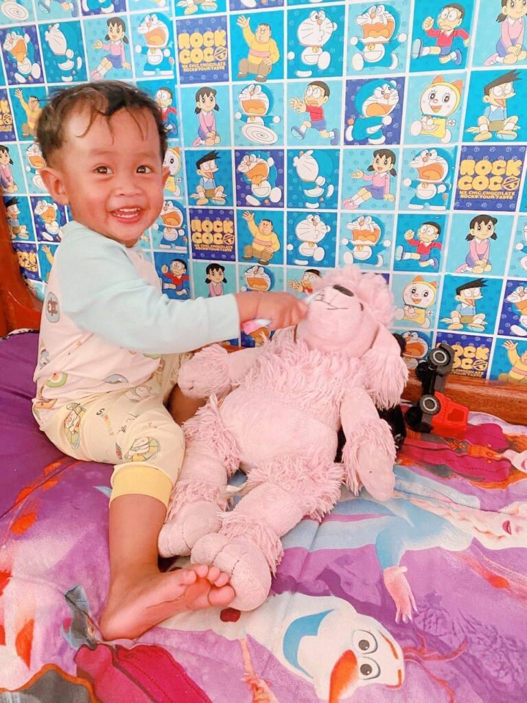 Smiling toddler brushing a pink stuffed poodle's teeth, demonstrating a clever parenting hack for when a toddler won't brush teeth.