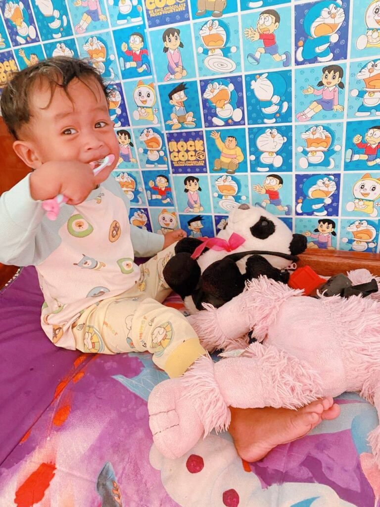 Toddler happily brushing his own teeth using a bright pink toothbrush, showing how the right tools make teeth brushing fun.