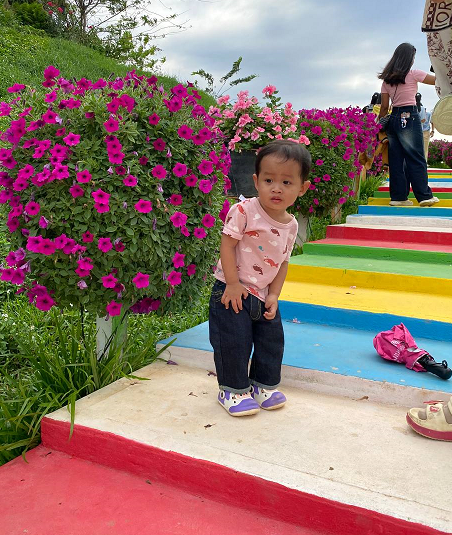 Toddler pausing while climbing steep colorful rainbow stairs, holding onto his pants, looking tired.