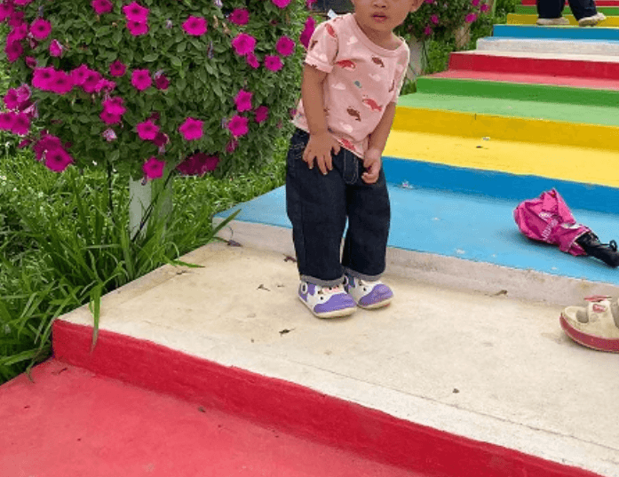 A toddler boy focuses intently on climbing bright yellow, blue, and red rainbow stairs at a tourist attraction in Siem Reap.