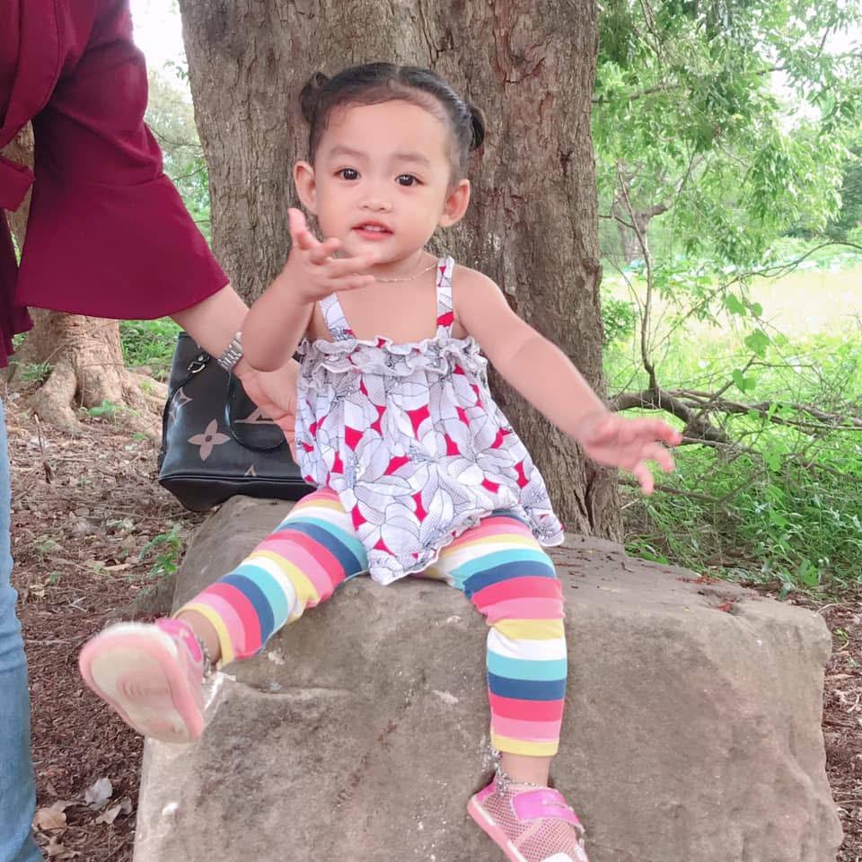 A three-year-old girl in rainbow leggings sitting on a rock at Ek Phnom Temple in Cambodia after successfully climbing it.