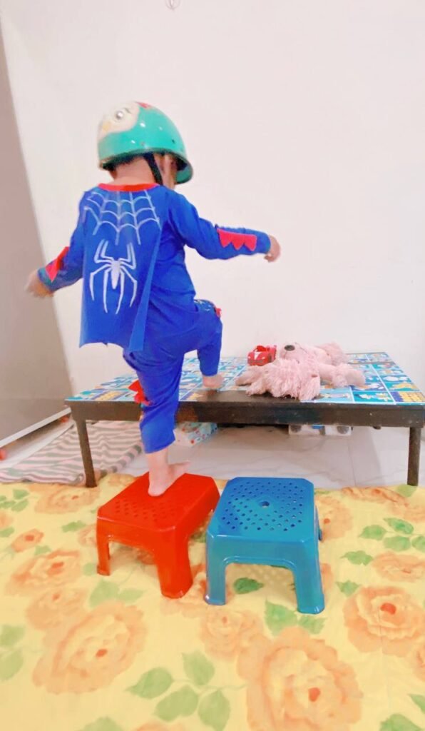 A toddler stepping from a red plastic stool onto a coffee table during an indoor obstacle course activity.