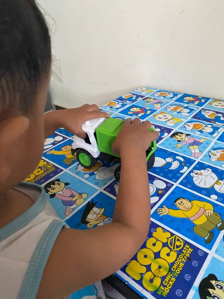 A toddler focusing intensely on aligning the hinges of a toy truck to fix it.