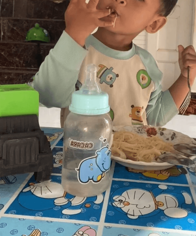 Toddler eating pasta with his fingers while holding a fork in the other hand.