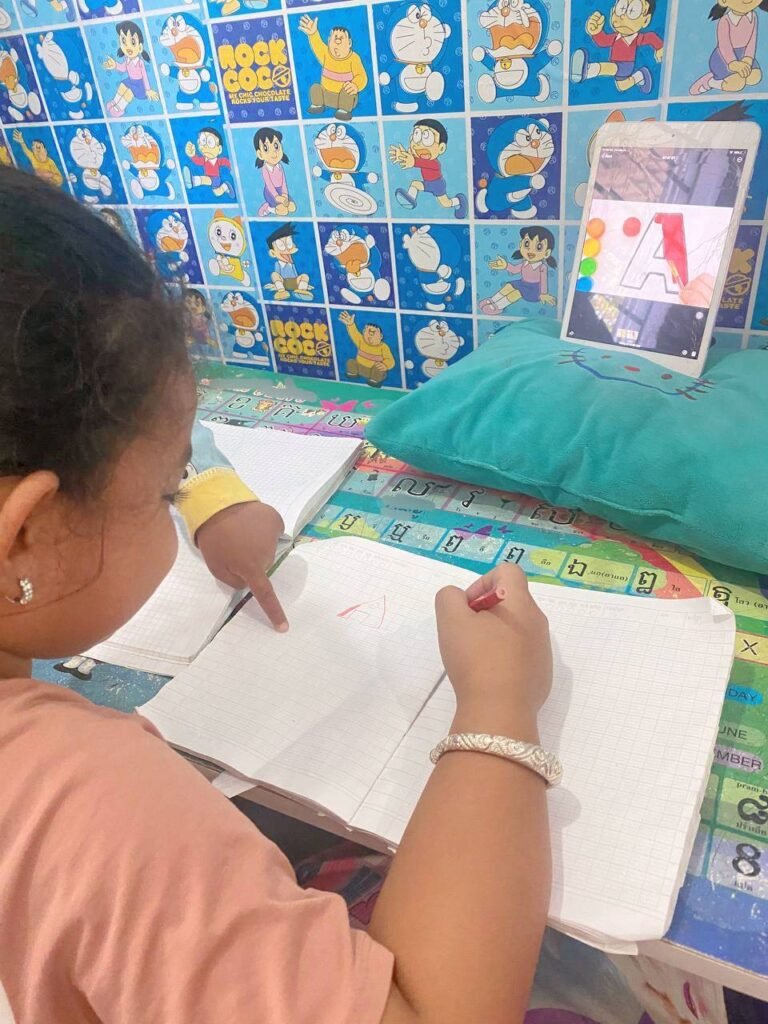 Close up of toddler pointing at the letter A in a notebook next to an iPad tracing app.