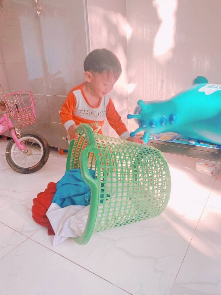 Toddler playing inside a green laundry basket as part of a game to wash his favorite clothes.