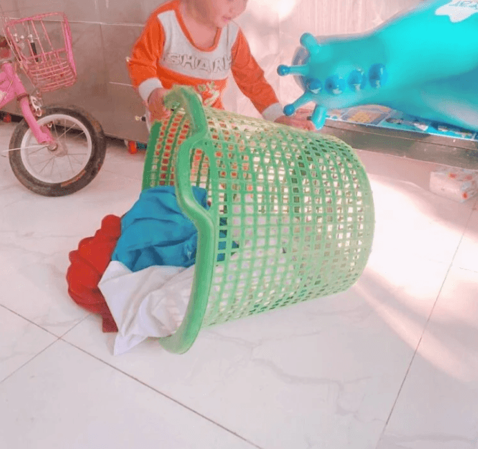 Toddler playing with a green laundry basket to help put his clothes in the wash as part of a bedtime routine.