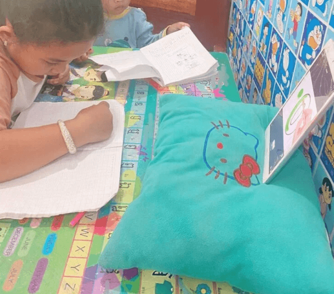 Toddler boy sitting quietly next to his older sister at a small desk, observing her while she practices her writing.