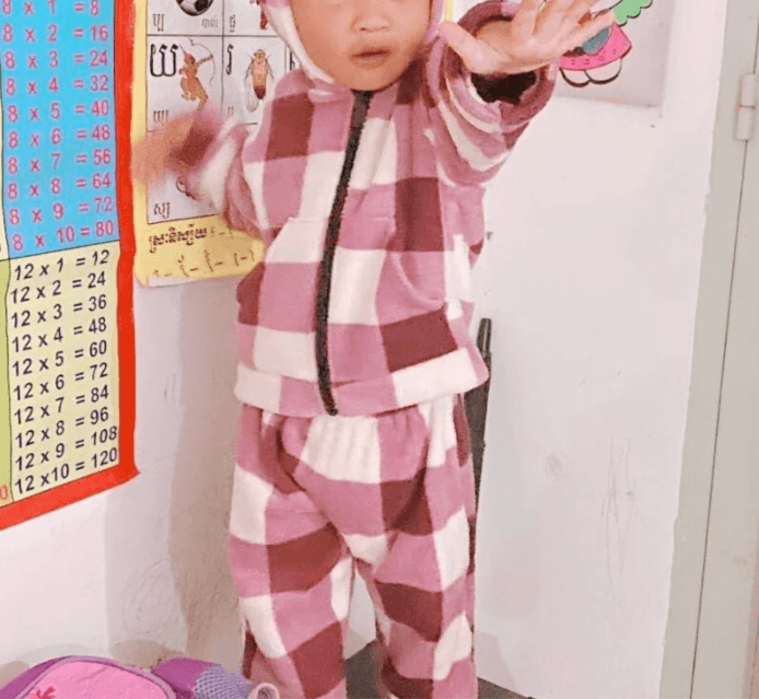 A toddler in pink striped pajamas waving hands in front of a colorful wall number chart, demonstrating fun counting games.