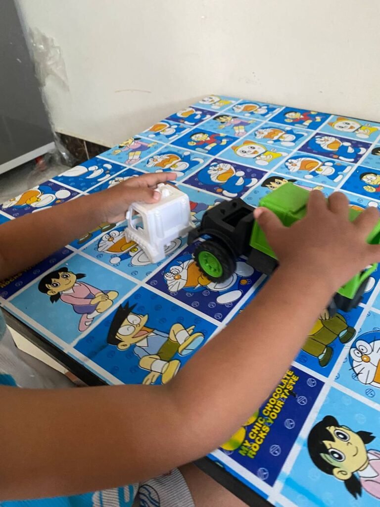 A young child trying to force a white truck cabin onto the wrong part of a green recycling truck.