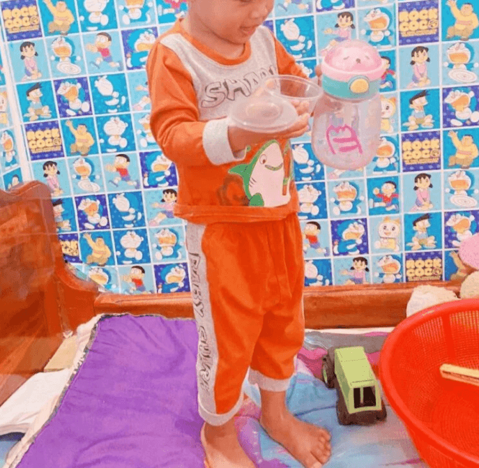 Toddler wearing his favorite orange shark outfit standing in front of a wall with blue Doraemon stickers.