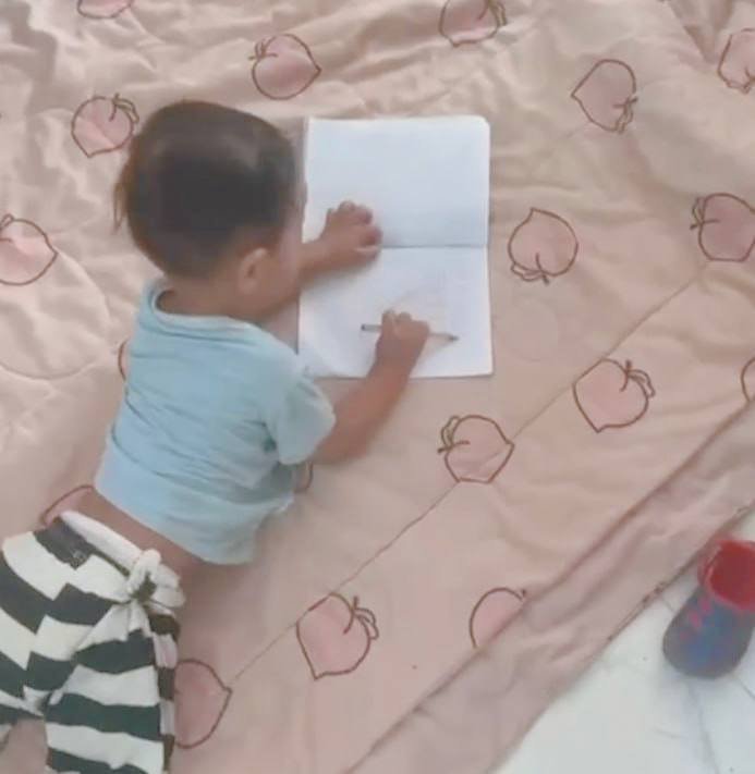 A two-year-old boy demonstrating the "fist grip" by holding a pencil with his whole hand while drawing.