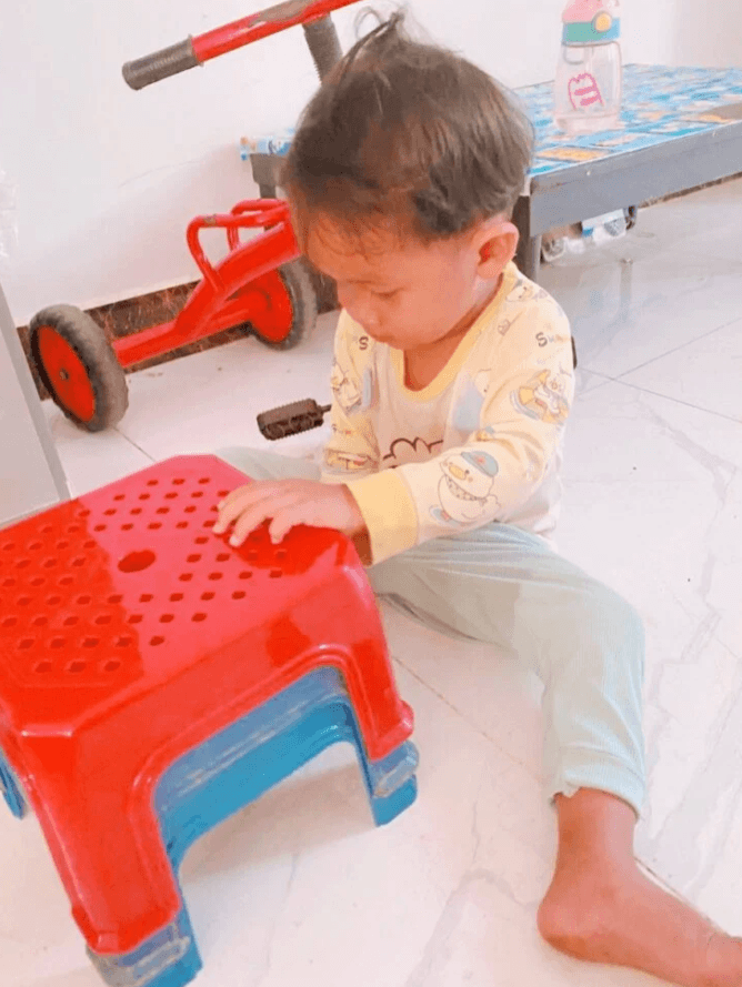 A 2-year-old toddler engaging in open-ended play by exploring nested red and blue plastic stools on the floor.