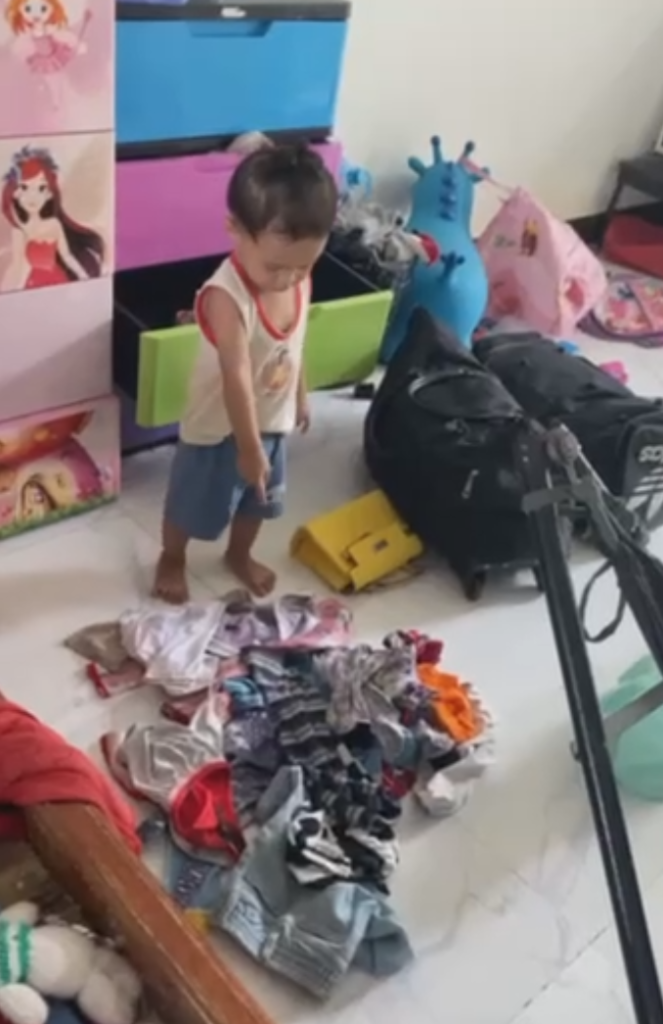 Two-year-old boy pointing proudly at a large pile of clean laundry he emptied onto the floor.