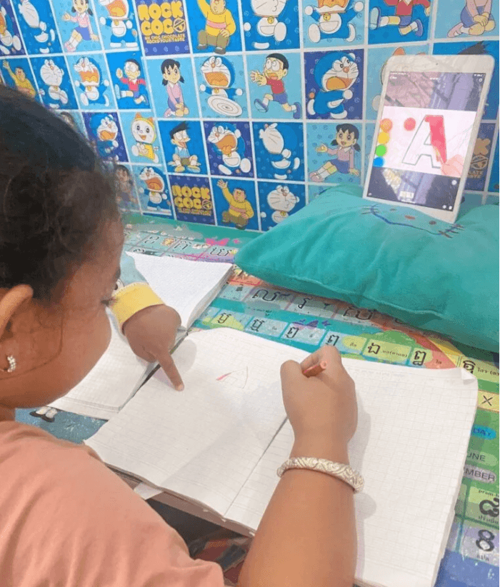 Toddler's hand pointing directly at the letter A that his older sister just drew in her notebook.