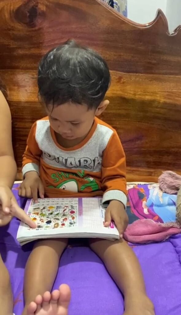 A toddler using his index finger to point at a specific image in a vocabulary grid book to learn new words.