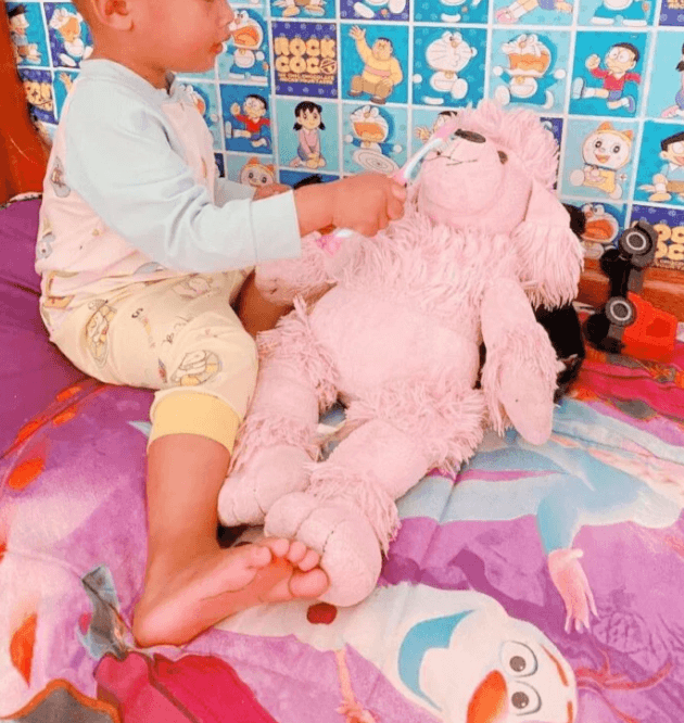 A toddler focused on carefully brushing the teeth of a pink stuffed animal.