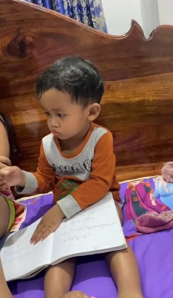 Toddler holding a notebook with handwritten notes, mimicking the act of reading and turning pages.