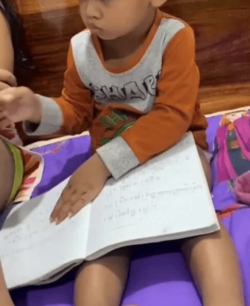 A young boy resting his hand on an open notebook full of scribbles, demonstrating early print awareness.