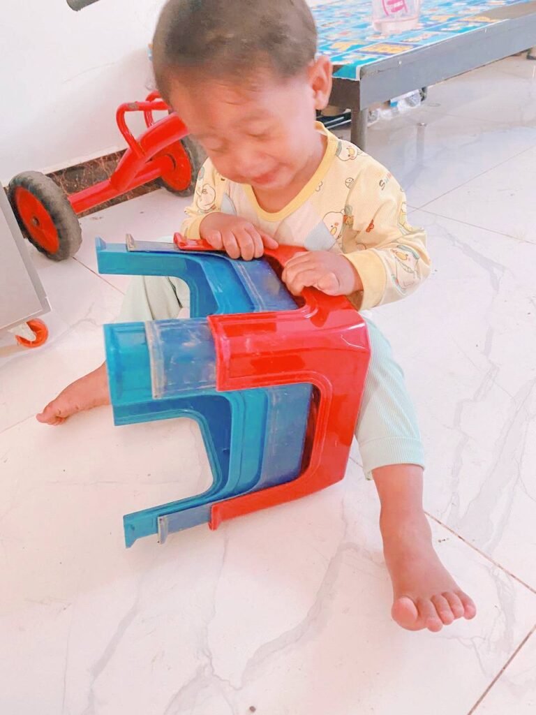Toddler trying to pull apart two stuck plastic stools, showing effort and concentration.