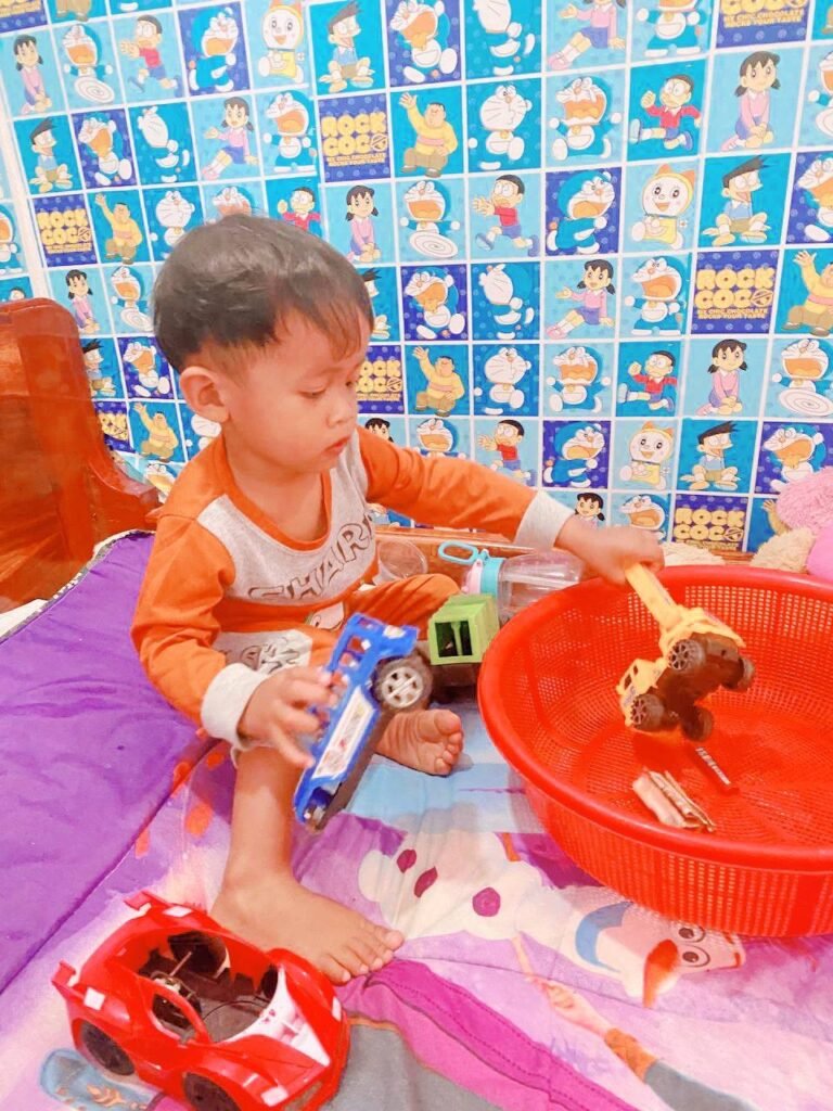 Toddler playing with construction trucks and a red basket, wearing the same orange outfit for sensory comfort.