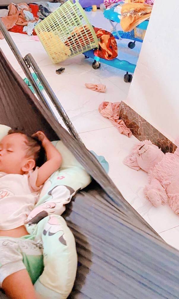 A toddler sleeping in a portable camping hammock in a messy living room with a laundry basket, used as a sensory overload hack.