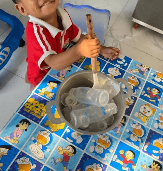 Close up of an aluminum pot filled with empty plastic milk bottles and lids for a pretend cooking activity.