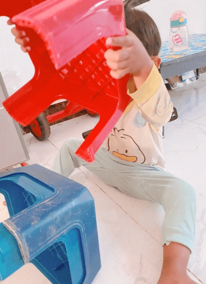 A toddler holding a red plastic stool up to his face and looking through the ventilation holes during imaginative play.