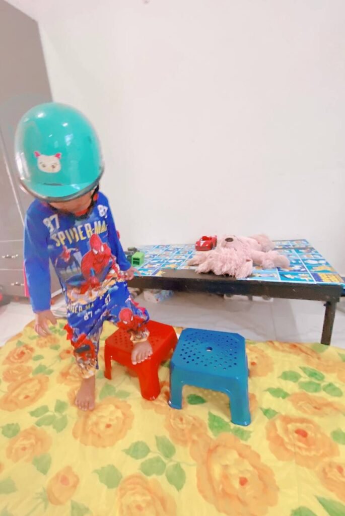 Toddler wearing a blue bicycle safety helmet and Spiderman pajamas walking on a play mat.