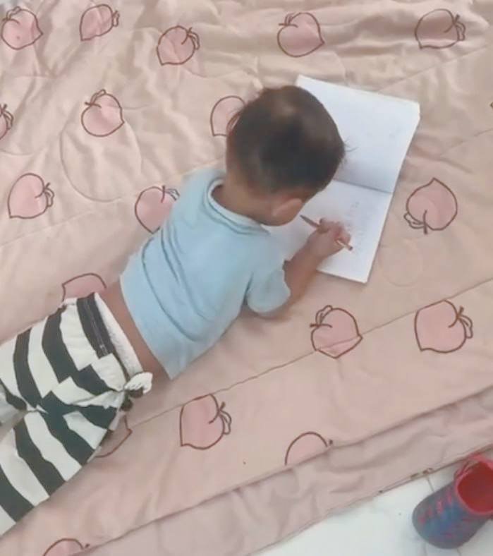 Toddler drawing while lying on his stomach on the floor to build core strength.