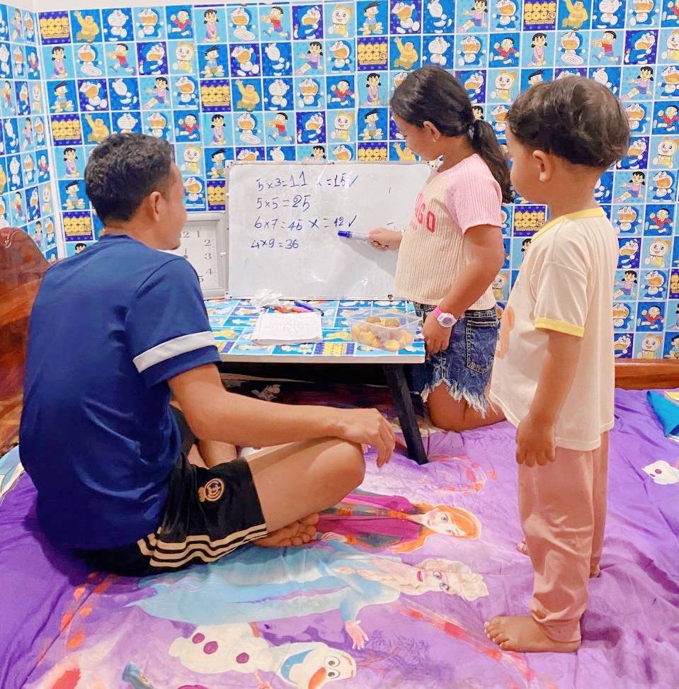 Father helping 7-year-old daughter with math homework on a whiteboard at home.