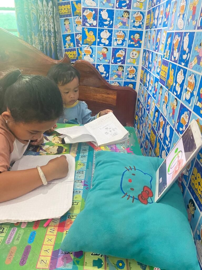 8-year-old girl focusing on homework at a small table while her toddler brother watches.