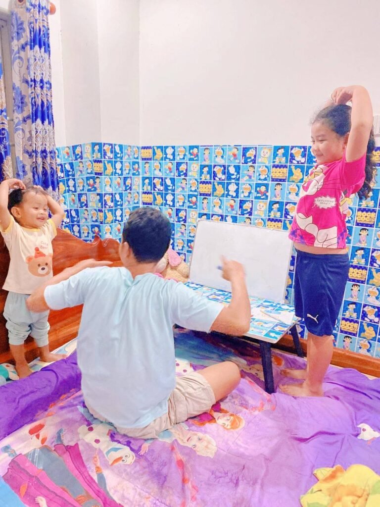 Father and two children relaxing in a blue Doraemon-themed study corner during homework time.