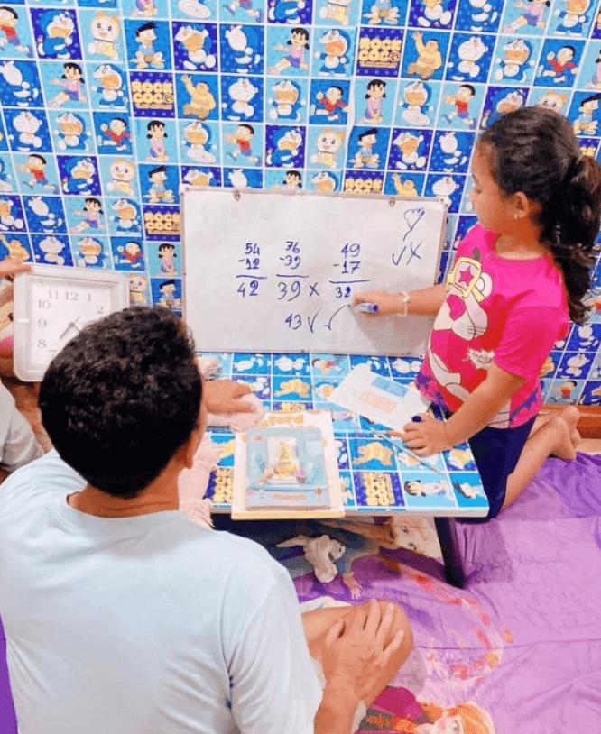 A father holding a square clock while his daughter corrects a subtraction math problem on a whiteboard.