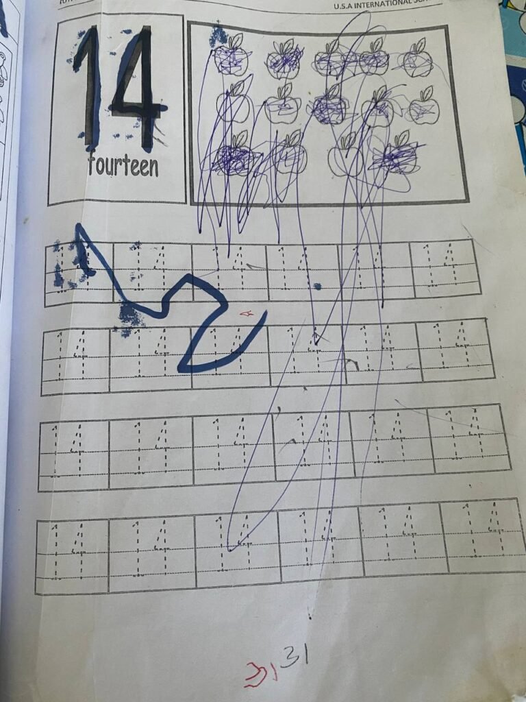 Math worksheet with number 14 covered in blue scribbles showing child's writing fatigue.