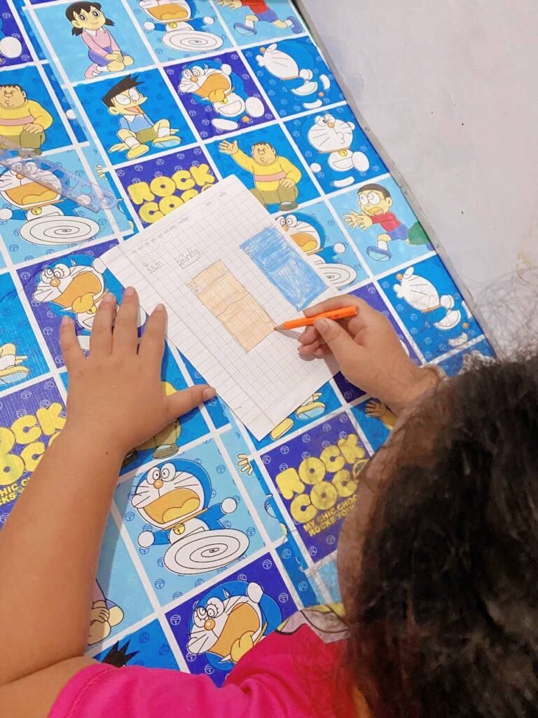 Child using colored pencils to fill in a progress chart on a low study table.