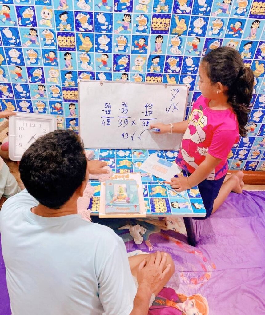 Young girl correcting a subtraction math error on a whiteboard while her father watches.