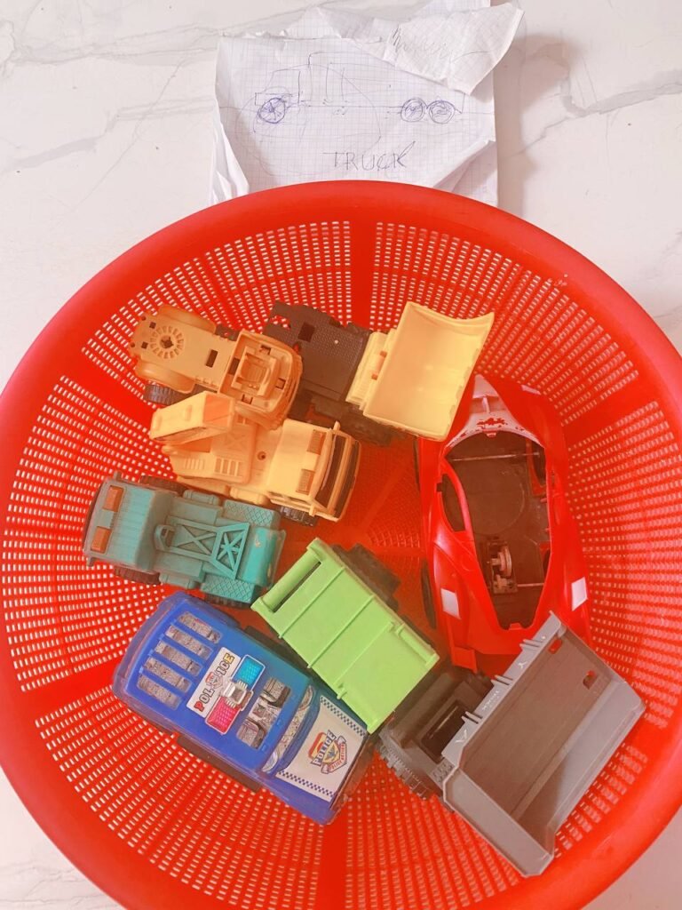 Red plastic toy basket filled with organized toy cars, trucks, and a yellow excavator.