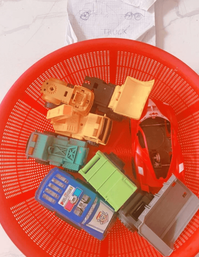 Red plastic toy basket filled with organized toy cars, trucks, and a yellow excavator.