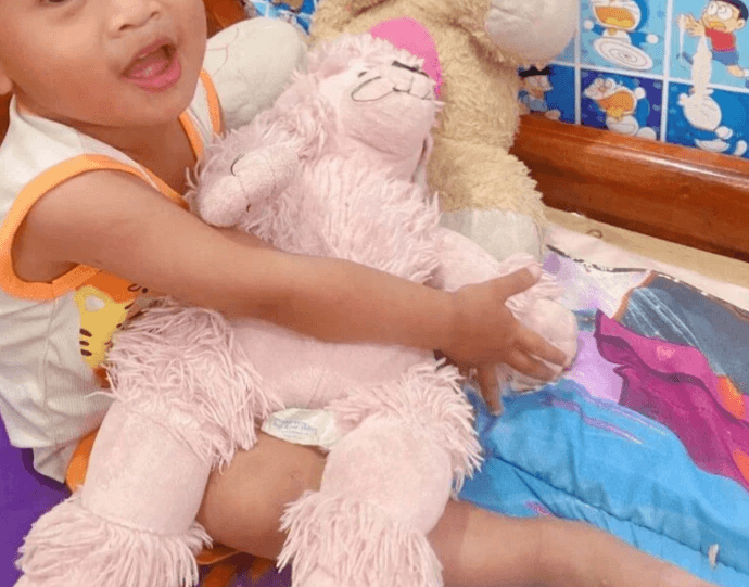A toddler boy happily hugging a large pink stuffed poodle toy to practice gentle hands.