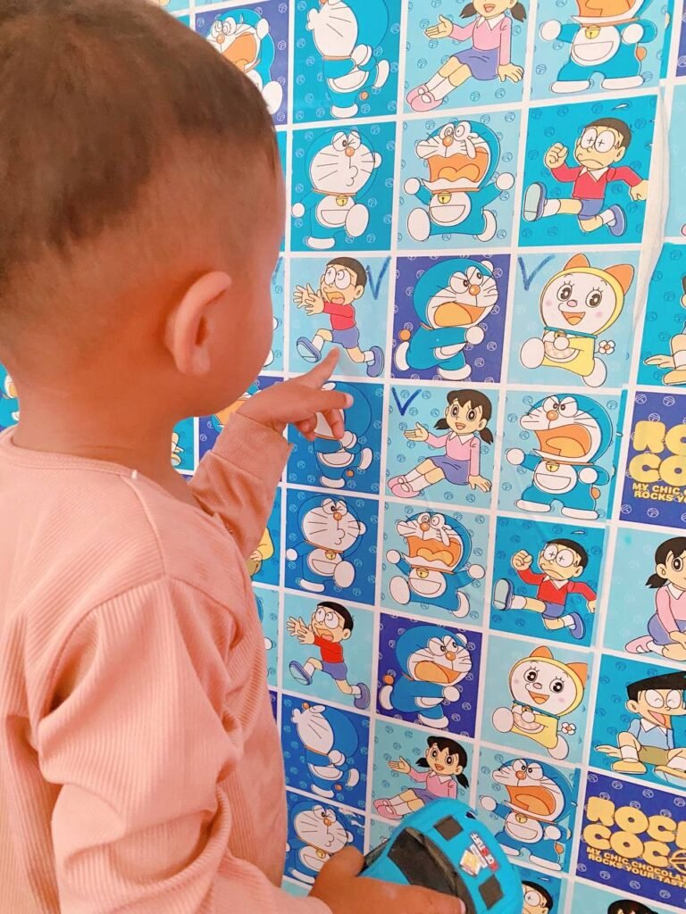 Toddler pointing to a wall decal of a cartoon character running and screaming, used to teach about tantrums.